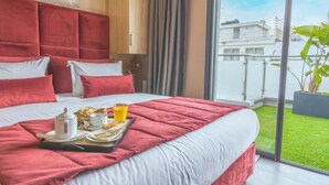 Une chambre d’hôtel moderne avec un grand lit, un plateau de petit-déjeuner et une vue sur la ville grâce à de grandes fenêtres.