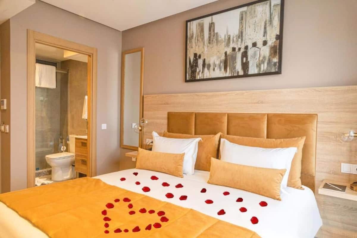 A hotel room with a bed, a large mirror, and a cityscape painting on the wall.