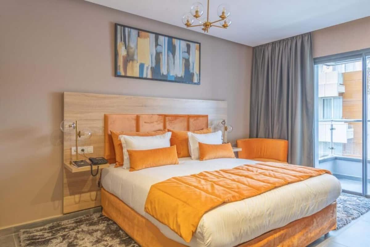 A modern hotel room with a large bed, a nightstand, a telephone, and a painting on the wall.