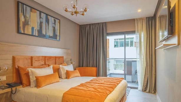 Une chambre d’hôtel avec un grand lit, un bureau avec un téléphone, un tableau au mur et un balcon avec des rideaux.