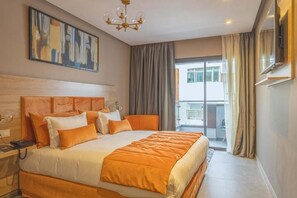 Una habitación de hotel con una cama grande, un escritorio con teléfono, un cuadro en la pared y un balcón con cortinas.