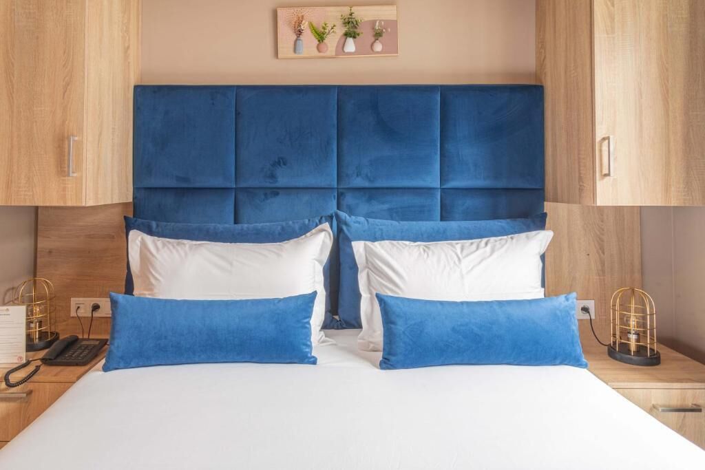 Habitación de hotel con una cama grande, dos mesitas de noche, un cabecero de madera y una planta en la pared.