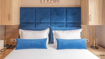 Habitación de hotel con una cama grande, dos mesitas de noche, un cabecero de madera y una planta en la pared.