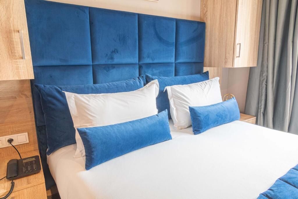 Habitación de hotel con una cama grande, un cabecero azul y una mesita de noche de madera con un teléfono.