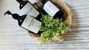 Drie flessen douchegel in een rieten mand met een bloemstuk.