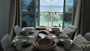 Een eetruimte met een tafel voor zes personen, grote ramen met uitzicht op zee, en een hangende lamp.