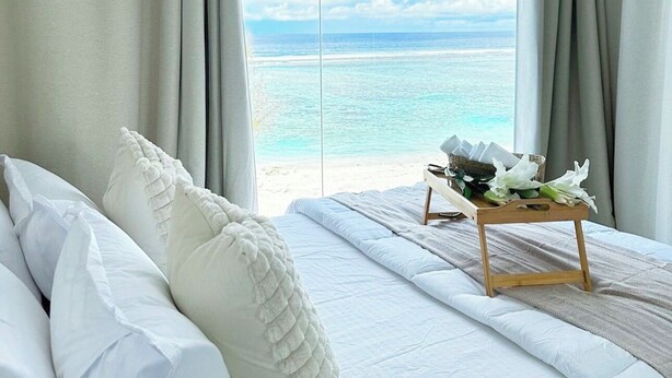 Een slaapkamer met een bed, gordijnen en uitzicht op de oceaan.