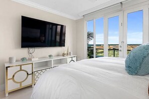 Een slaapkamer met een groot bed, een aan de muur bevestigde televisie, een witte console tafel en een balkon met uitzicht.