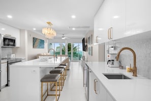 A modern kitchen with a central island, bar stools, a large window, and a view of greenery.