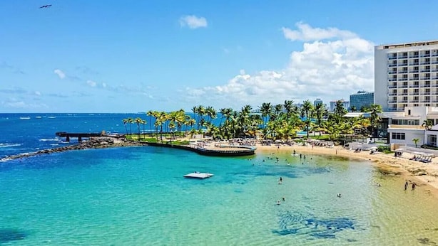 A coastal resort with a beach, palm trees, and a pier. - Oceanview Penthouse · Pool · Water Backup (San Juan)