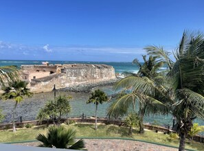 A coastal fortification with a view of the ocean, palm trees, and a paved walkway. - Designer Oceanview Penthouse & Pool - Condado (San Juan)