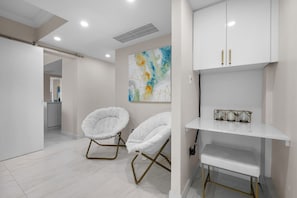 A modern, minimalist room with two white, cushioned chairs, a white shelving unit, and a colorful abstract painting on the wall. - Oceanview Penthouse · Pool · Water Backup (San Juan)