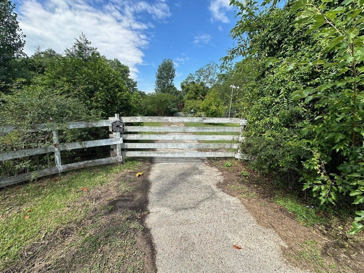 A gravel path leading to a wooden gate with a sign, surrounded by lush greenery.