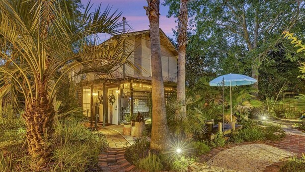 Une maison à la façade en verre, entourée d’une végétation tropicale et bordée d’un chemin de gravier.