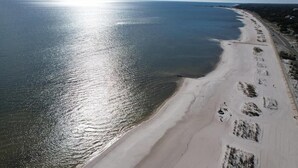 Une vue aérienne d’une plage, avec un ciel dégagé, une rive sablonneuse et une mer calme.