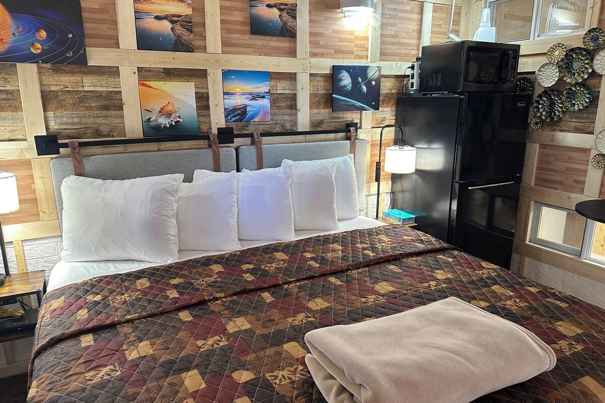 A neatly made bed with a patterned bedspread and a folded blanket, a wooden headboard, and a wall with framed pictures.