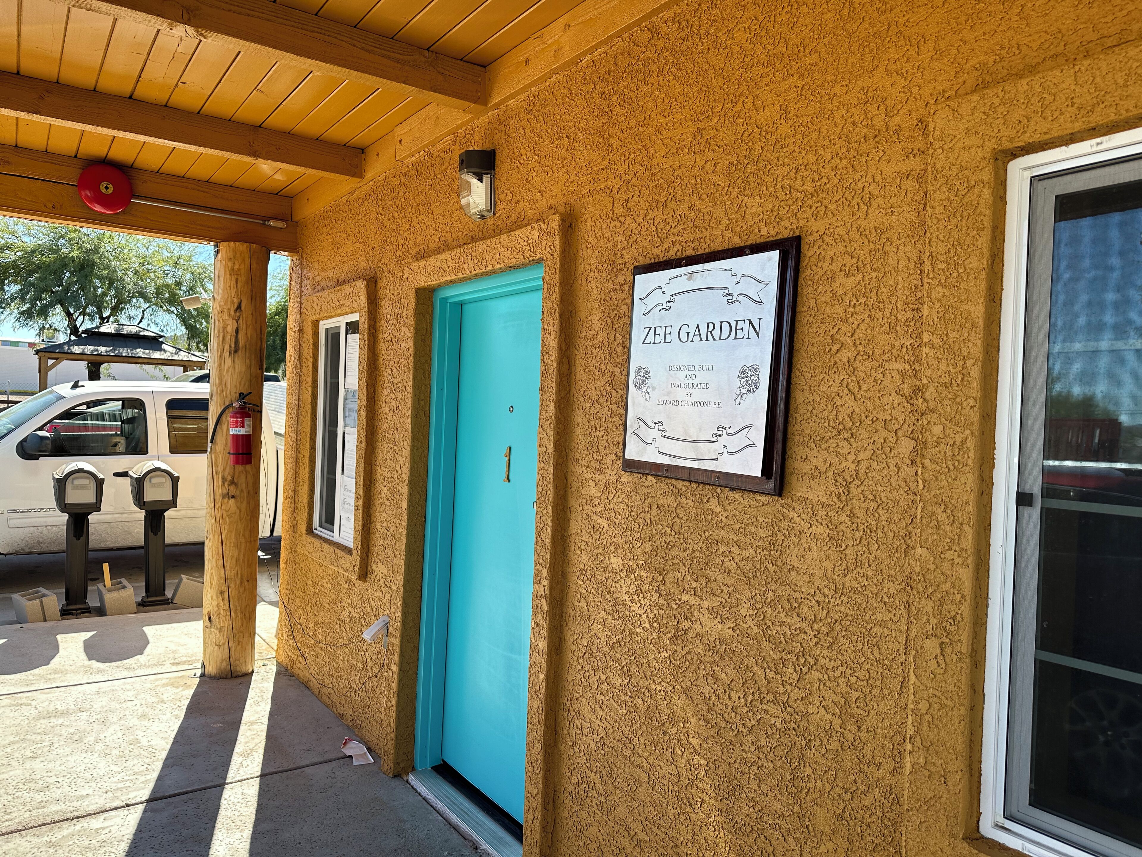 A building with a turquoise door, a framed sign reading "Zee Garden," and a wooden ceiling.