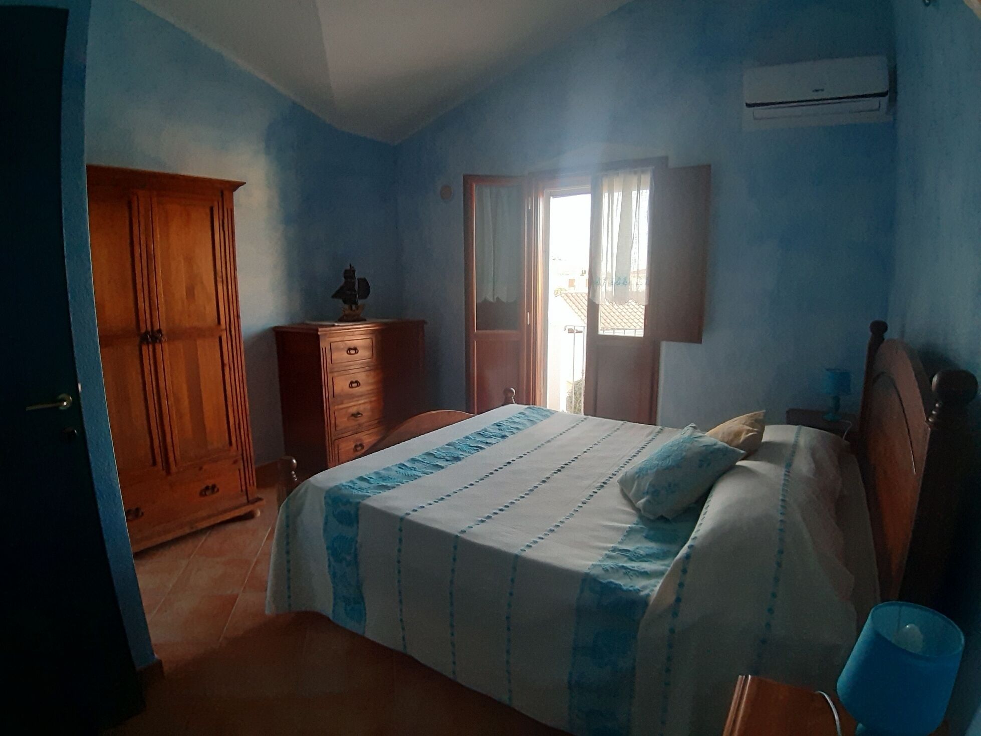 A bedroom with a bed, dresser, wardrobe, and an air conditioning unit.