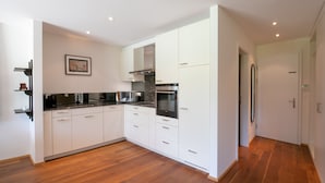 A modern kitchen with white cabinetry, a black countertop, and a wooden floor.