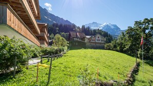 A traditional chalet with a wooden balcony, a green field, and a mountain backdrop.