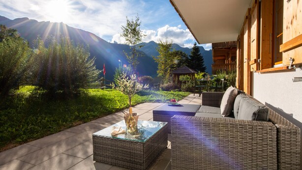 A patio with wicker furniture, a glass-top table, and a view of mountains.