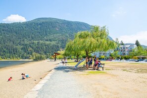 Una playa con un parque infantil, un sendero y vistas a una montaña boscosa.