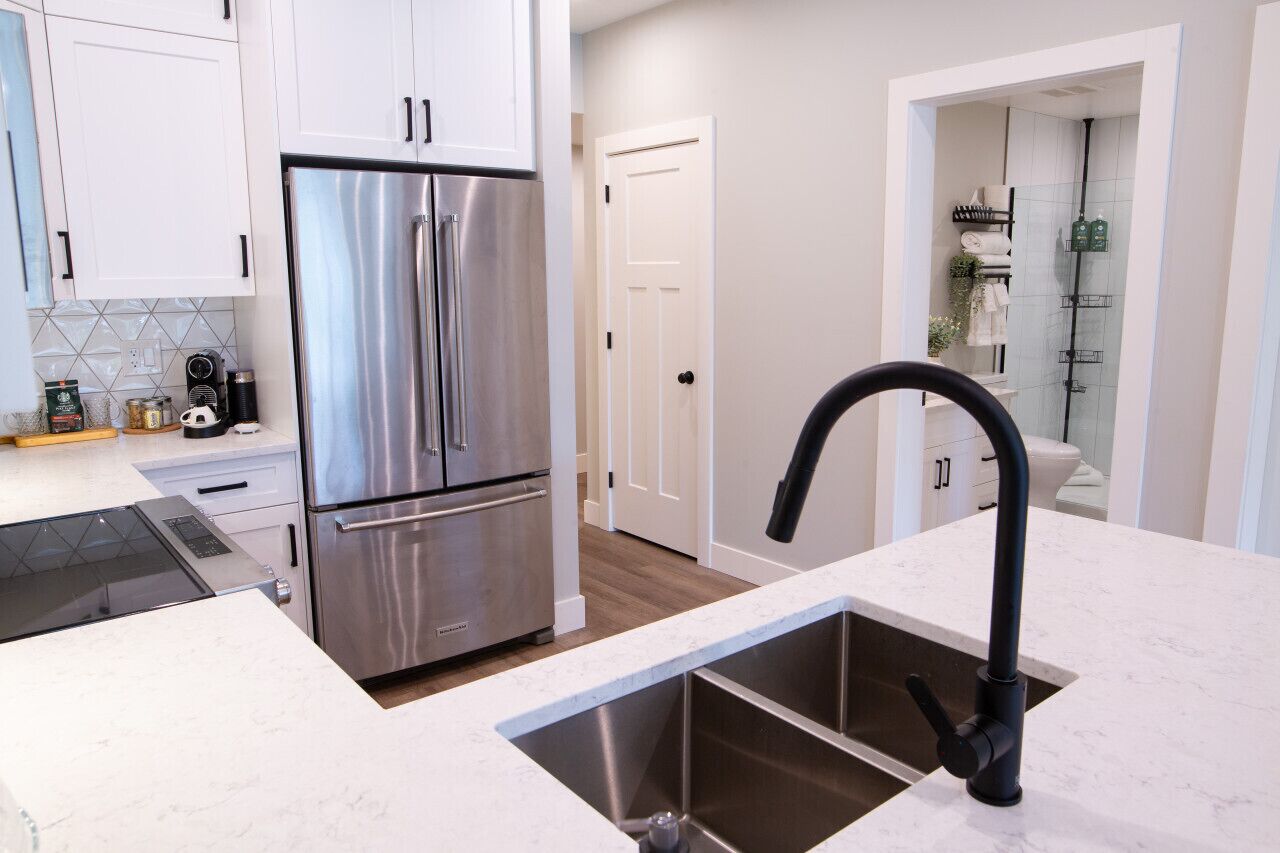 A modern kitchen with stainless steel appliances, a black faucet, and white cabinetry.
