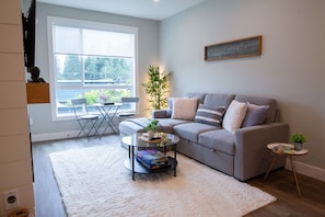 A living room with a grey sofa, a white rug, a small round coffee table, and a window with a view of a garden.