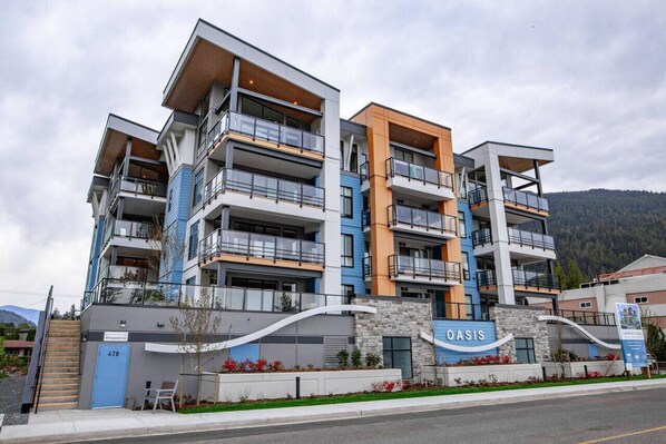 A multi-story hotel with balconies, a sign reading 'OASIS,' and a view of a mountain.