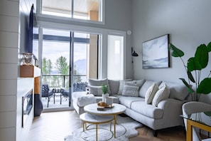 Een moderne woonkamer met een grijze bank, een ronde salontafel en een open haard.