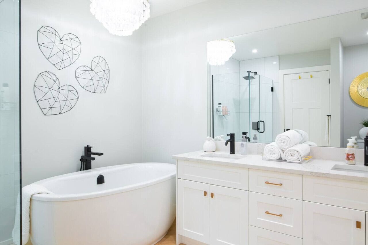 A modern bathroom with a freestanding bathtub, a large mirror, and decorative wall art.
