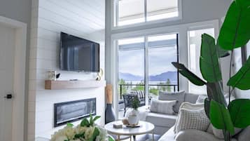 A modern living room with a fireplace, a flat-screen TV, and a large window offering a mountain view.