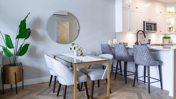 A modern kitchen with white cabinetry, a central island with bar stools, and a dining table with chairs.