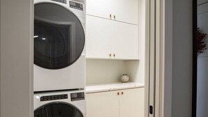 Een wasserijruimte met twee gestapelde wasmachines en een wit kastje met decoratie erboven.
