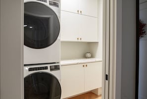 A laundry room with two stacked washing machines and a white cabinet with a decorative item on top.