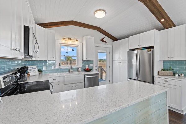A modern kitchen with white cabinetry, stainless steel appliances, and a large island.