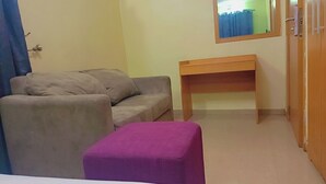 A room with a grey sofa, a wooden table, and a purple ottoman. - Ikad Hotel and Suite Borno Way (Lagos)
