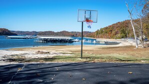 A basketball court with a clear view of a lake and dock structures in the background. - Breathtaking Lakeside 2-Bedroom Cabin on Beautiful Dale Hollow Lake #9! (Byrdstown)
