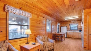 A cozy cabin interior with wooden walls and floors, a dining area with a table and chairs, and a kitchen with cabinets and a window. - 2 Bedroom lakeside to Dale Hollow Lake! (Byrdstown)