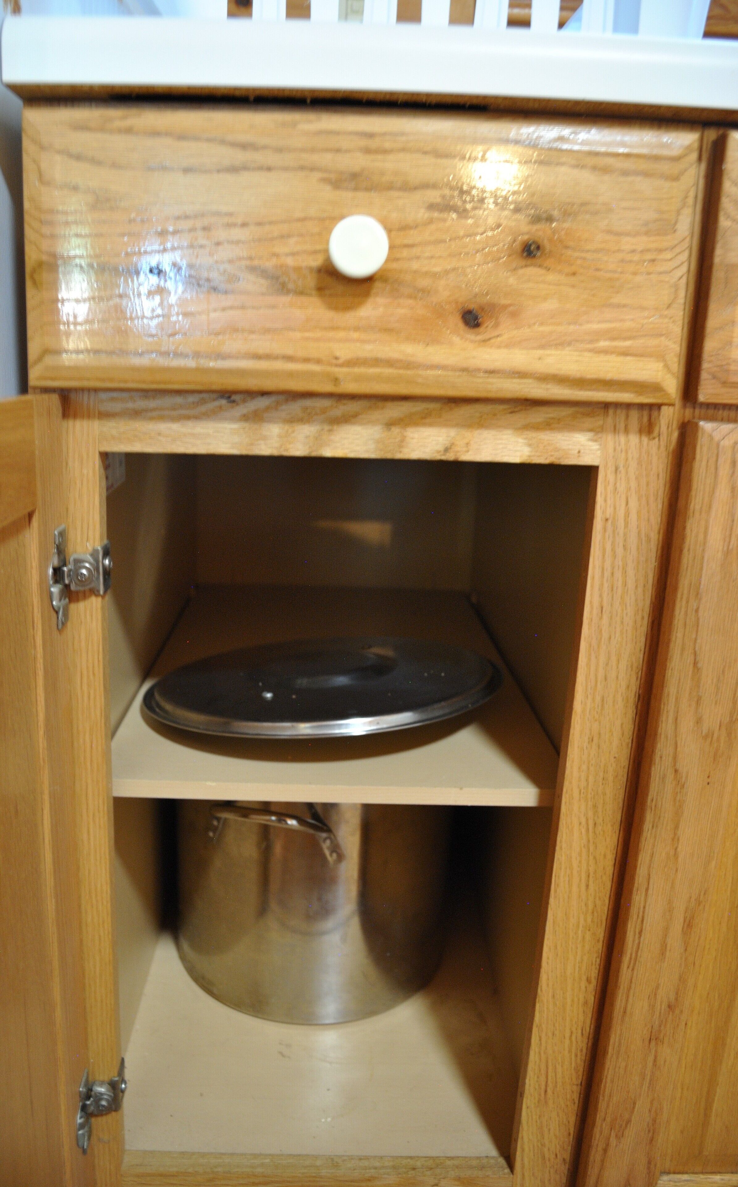 Un gabinete de madera con tapa abatible, una olla de metal y un estante.