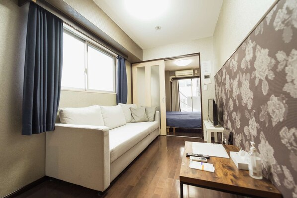A compact room with a sofa, a small table with a remote control, and a patterned wall. - アクセス&コスパ最高!徒歩 本町駅5分! 広々デザイナーズ1LDK、最大6人!902 (大阪市)