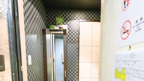 Un pasillo con un estampado de cuadros en la pared, una puerta adornada con una planta en la parte superior y un cartel de prohibido fumar en la pared.