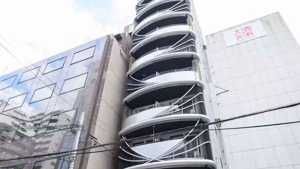 Un edificio de varios pisos con una fachada curva distintiva, una entrada visible y una bicicleta estacionada afuera.