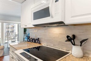 Una cocina con armarios blancos, microondas, placa de inducción y salpicadero.