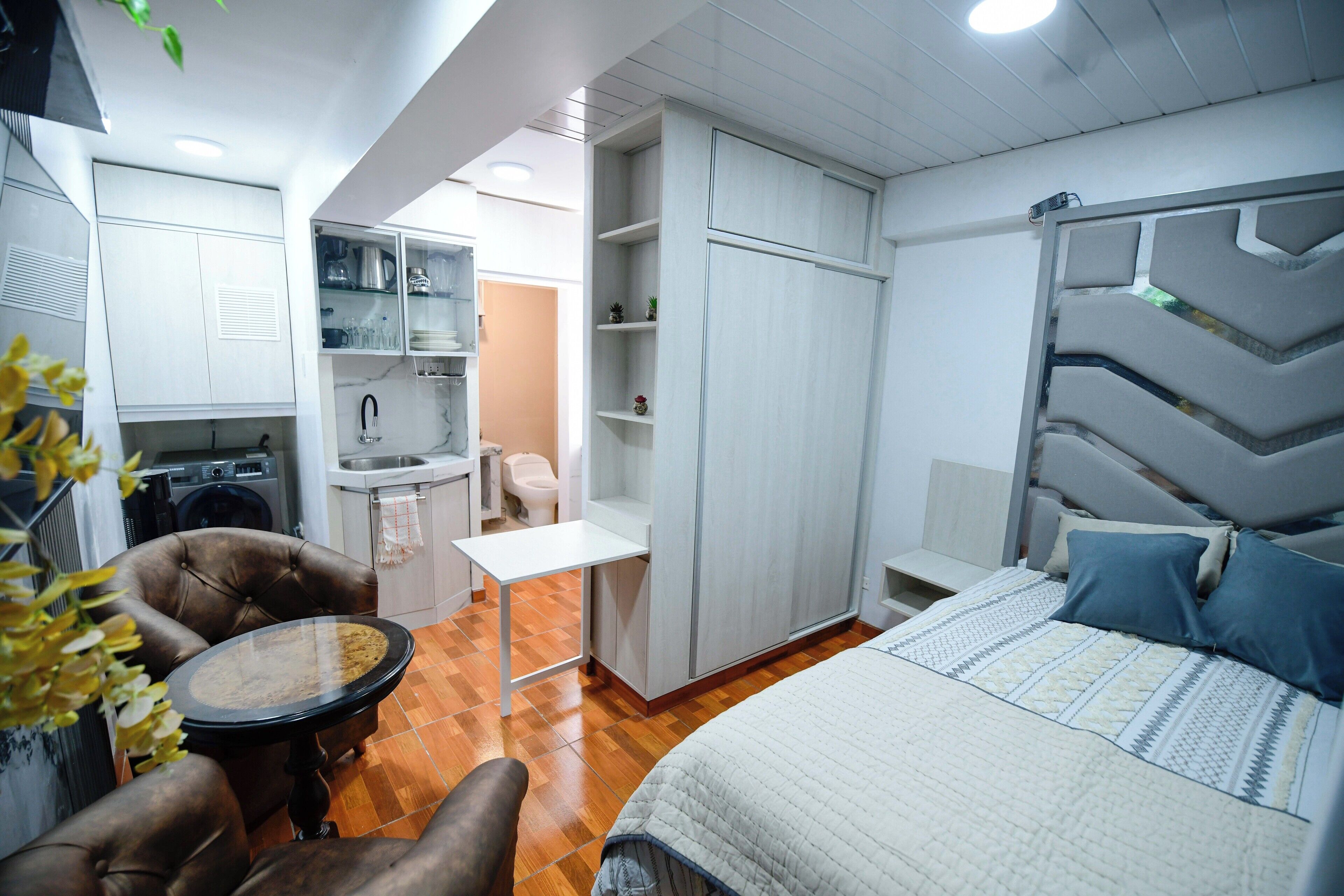 Habitació d'hotel senzilla amb llit, taula petita de dinar, sofà, zona de cuina equipada i bany.