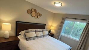 Un dormitorio con una cama, dos mesitas de noche con lámparas, una obra de arte en la pared y un ventanal con cortinas.