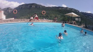 A swimming pool with clear blue water, surrounded by stone walls and a mountainous backdrop.