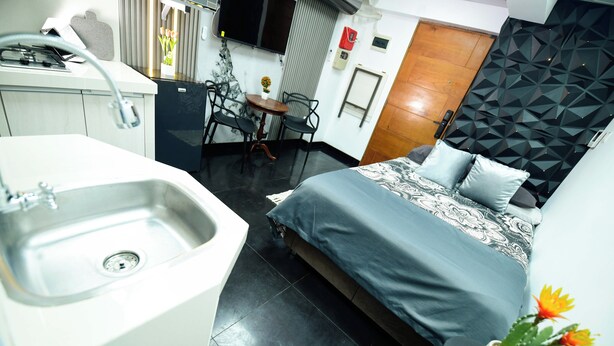 Habitación de hotel compacta con cama, una pequeña mesa con sillas, un lavabo y un panel decorativo en la pared.