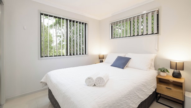 A bedroom with a large bed, two bedside tables, a nightstand, and a window with blinds. - Comfortable Rocklea 1BR | Near Shops | Parking | 173B2 (Rocklea)
