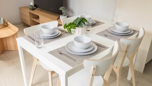 Une table à manger dressée avec de l’assiette, des bols et des verres blancs, entourée de chaises en bois.